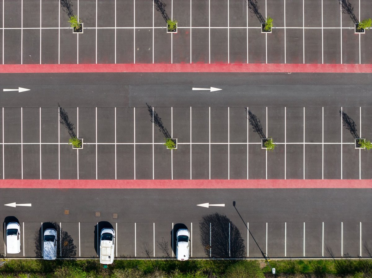 Straight down close up aerial photo of a car park in the city of York UK showing parking bays white lines directional arrows and small trees forming a strong geometric pattern on asphalt surface