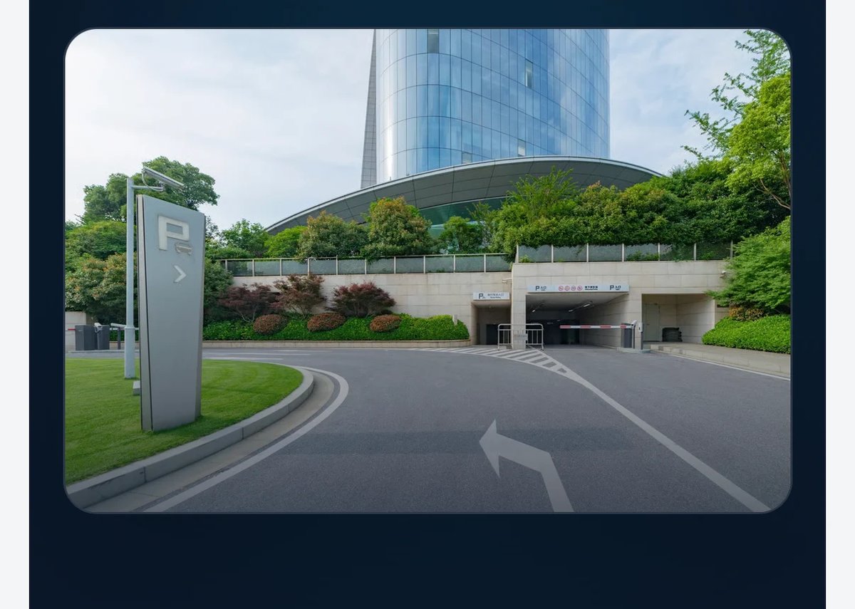 Modern parking garage entrance with curved architectural roof, modern tower building, green landscaping, and directional road markings